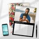 An A4 wall calendar for September 2025 with a sleek black design. The page features a joyful photo of a man and child on the beach, with a monthly grid below. A second calendar with a Christmas tree scene is partially visible underneath. A smartphone and pen are placed next to the calendars.