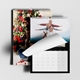 Two A4 wall calendars with a sleek black design. One displays a Christmas scene with a decorated tree, while the other shows a family outdoors with a page being turned. Both calendars feature monthly grids, spiral bindings, and hanging hooks.