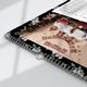 Close-up of an A4 wall calendar with black floral borders and silver spiral binding. The page shows a family Christmas photo, decorated with a 