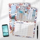 Two A3 photo calendars for 2025, one opened to January. The January calendar features your own image. A smartphone and pen are placed next to the calendars on a white desk, with space for notes in the month grids.