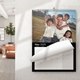 An A3 wall calendar for May 2025 with a sleek black design. The page features a family photo of a man with three children in a park, with a monthly grid below. The calendar is spiral-bound with a hanging hook and is displayed on a white wall in a modern room.