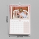 An A3 pink glitter-themed photo calendar displaying the July 2025 page. The picture shows a young child kissing a baby on a white bench. The calendar is wire-bound, measuring 420mm by 297mm, with a month grid layout.