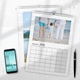Two photo wall calendars lie on a white surface next to a smartphone and pen. The top calendar is open to January 2026 and features a beach photo of a child holding hands with two adults. The calendar beneath shows a scenic image of a person standing beside a mountain lake. Both calendars have wire binding and white borders with a subtle wave pattern.