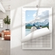 Wall calendar hanging on a white wall in a bright room, open to a scenic photo of two people standing by a lake with snow-capped mountains and pine trees in the background. The calendar features a wire binding and curved page design, with a minimalist layout and decorative line pattern on the border.