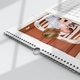 Close-up of a wall calendar showing a high-quality wire binding with a hanging hook, lying flat on a white surface. The featured photo displays a young child lovingly holding a baby on a rustic white bench in front of a red door. The page layout includes part of a calendar grid, with a modern, minimalist design and subtle line accents on the edges.