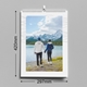Wall calendar displayed against a grey background, showing a couple holding hands and admiring a scenic lake and snow-capped mountains. Dimensions are marked: 297mm height and 210mm width, indicating standard A4 size. The calendar is wire-bound with a central hanging hook and a clean, white border featuring a subtle abstract line pattern.