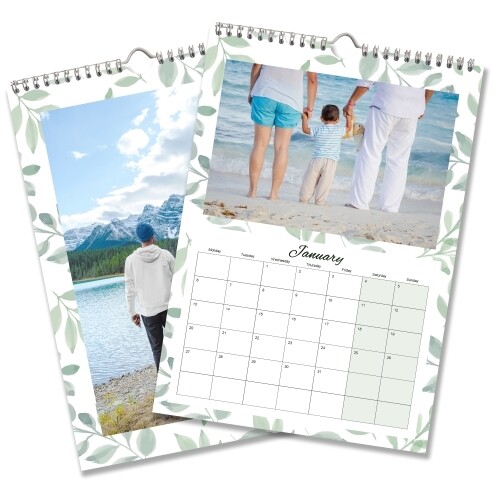 Two spiral-bound wall calendars with leafy borders. The top page shows January with a calendar grid and a photo of a child holding hands with two adults at the beach. The second page displays a person walking along a lake with snow-capped mountains in the background.