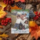 A personalised Christmas card featuring a man with two children outdoors, smiling and posing in casual clothing. The card is placed on a bed of autumn leaves, pinecones, and red berries, and reads, 