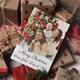 A personalised Christmas card featuring a family of three in festive sweaters. The man holds a baby on his shoulders while the woman smiles beside them, set against a decorated Christmas tree. The message reads, 