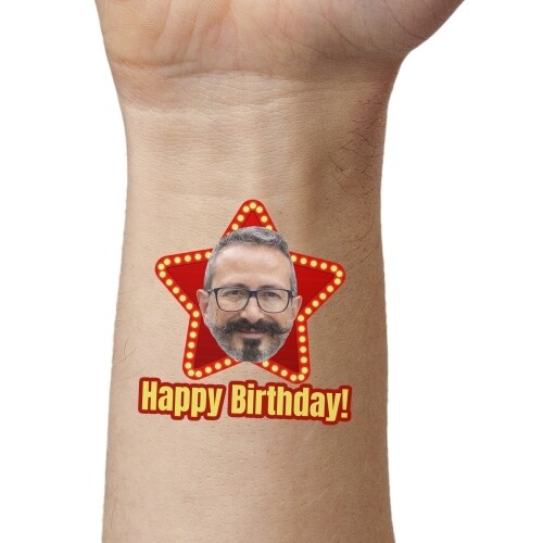 Close-up of a wrist displaying a red star-shaped temporary tattoo with a man's face and the bold text Happy Birthday! The tattoo adds a celebratory and fun detail to the skin.