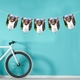 Image of personalised bunting with repeated pictures of a toddler holding hands with an adult, displayed against a bright teal wall, with a bicycle leaning nearby.