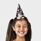 Smiling girl wearing a black personalised party hat featuring another young girl's face, decorated with pastel pink, green, and purple bubbles and the number 3, perfect for a third birthday celebration.