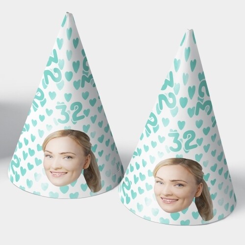 Two customised party hats with a white background featuring turquoise heart patterns, the number 32, and a personalised photo of a smiling woman. The hats are displayed upright side by side. Perfect for birthdays or celebrations.