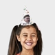 Smiling young girl with long dark hair wearing a personalised party hat featuring a colourful polka dot design, the text Brain's 80, and a photo of an elderly man in a flat cap. The hat is cone-shaped and sits on her head against a plain background.