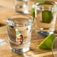Shot glass decorated with a personalised vinyl sticker showing a smiling man's face wearing a green party hat with the number 30. Surrounded by lime wedges and salt on a wooden surface, perfect for customised birthday party drinks or stag do celebrations.