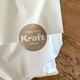 Round 30mm personalised Kraft label with white print sealing a white paper bag on a wooden surface. The custom brown sticker has a striped texture and bold white text reading White Print Kraft Labels, ideal for packaging, takeaway bags or small business branding.