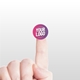 Close-up of a hand holding a small, personalised circular label with a custom logo on the fingertip, set against a light background. The label is pink and purple with the text Your Logo in white.