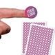 Close-up of a fingertip holding a small circular sticker with the words Your Logo on it in white and pink. Two sheets filled with similar logo stickers are placed in the background.