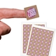 Close-up of a hand holding a small square custom sticker with bold text in pink, white, and yellow on a kraft background. Two sheets of identical stickers are displayed below. Perfect for personalised labelling and branding.