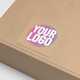 Brown kraft box with a square custom sticker on the lid, featuring bold text in pink, white, and yellow on a kraft background. Perfect for personalised packaging and branding solutions.