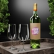 Green wine bottle with a personalised kraft label featuring the text Your Logo in bold pink and white. The bottle is displayed on a stone tray alongside two empty wine glasses, with greenery in the background, ideal for customised product branding.