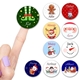 A collection of round personalised Christmas stickers featuring festive designs such as elf legs, Santa, reindeer, gingerbread man, snowman, and gnome. Names include Kit, Alfie, Daisy, Alistair, Lara, Maisy, Jack, Harry, Arthur, and Alexis. A finger with lavender nail polish points to the Kit sticker.