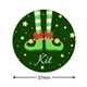 37mm round personalised Christmas sticker featuring green elf shoes with red trim and gold bells. The background is dark green with yellow stars, and the name Kit is written in white at the bottom.