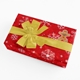 Red gift box with white snowflake patterns, wrapped with a large gold ribbon. A personalised gingerbread man sticker labelled 