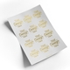 A sheet of custom transparent foil stickers featuring a gold-foil design that reads Your Design Here. The stickers are arranged in a grid pattern on a white backing sheet, reflecting light for a premium look. The sheet is slightly curled at the corner.