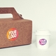 Brown cardboard takeaway box with a sturdy handle and a white disposable coffee cup, both featuring personalised circular logo stickers. The stickers have a gradient design with bold white text. Ideal for branding food packaging, cafes, and events.